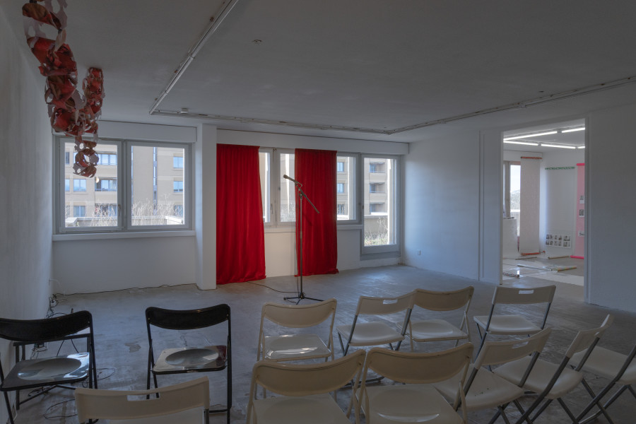 Exhibition view, Sven Gex, celebratory, Halmet, Zürich, 2025. From left to right: Sven Gex, garland for ‚celebratory‘ (maid-of-all-work character), 2025, aid-of-all-work character), 2025 hand cut printed pictures, staples ; Sophie Becker, Setup of “Ronnie’s World”, Performance during the opening night ; Sven Gex, celebratory, 2025, gift wrapping paper, nails, glass, printed images from the ‚character fitting‘ series 2021-ongoing